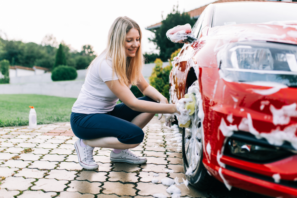 Eine junge Frau wäscht die Felgen eines roten Autos mit einem Schwamm.