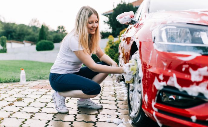 Eine junge Frau wäscht die Felgen eines roten Autos mit einem Schwamm.